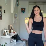 Smiling woman in activewear lifting dumbbells at home for a healthy lifestyle.