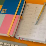 Colorful 2025 planner and calendar with pen on a bright yellow desk.